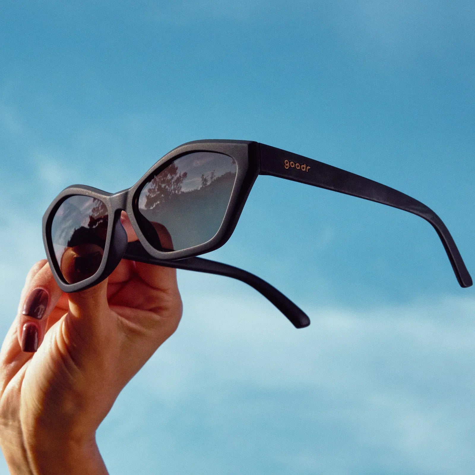 Dark purple sunglasses held against blue sky showing classic frame design