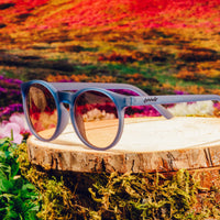 Round sunglasses with light blue frames and gradient reflective lenses on wooden surface