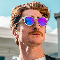 Round sunglasses with clear frames and blue-purple mirrored lenses worn by person outdoors