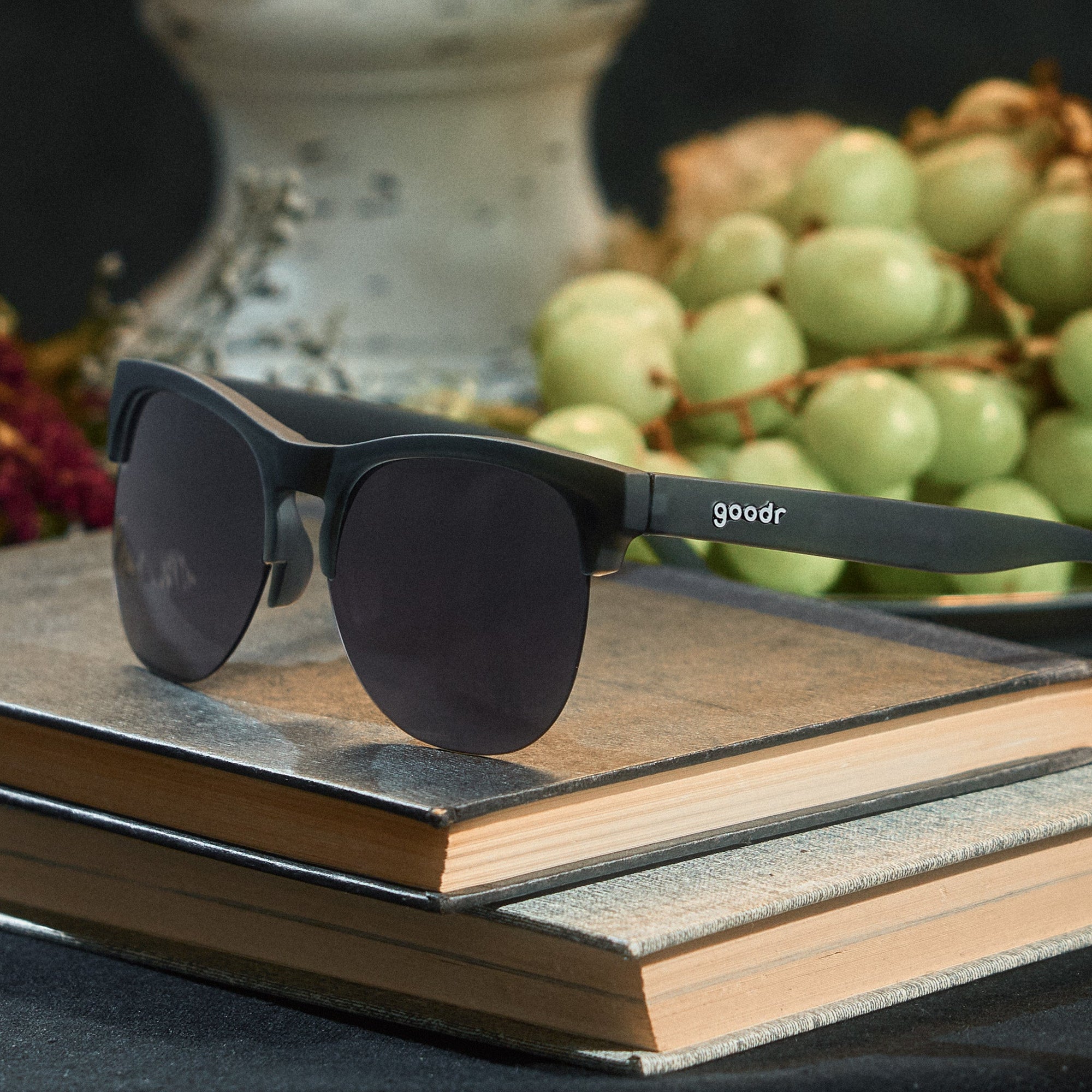 Black half-frame sunglasses with dark lenses positioned on stacked wooden books