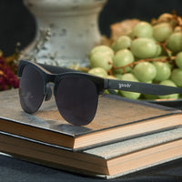Black half-frame sunglasses with dark lenses positioned on stacked wooden books