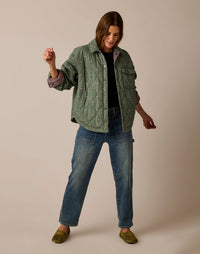 Quilted reversible shirt jacket in sage green with embroidered details, worn open over black top and jeans