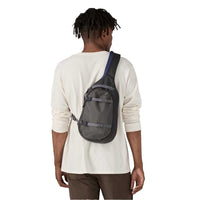 Sling bag worn across back on model, dark gray with navy strap, rear view