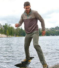 Man stepping on rocks by a lake wearing a colorblock knit pullover with quarter-snap collar