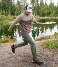 Man running outdoors in colorblock knit pullover with quarter-snap collar, green pants, near forest lake