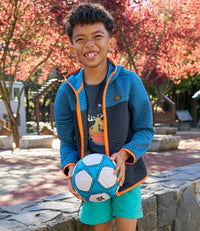Boy wearing blue colorblock zip-up hoodie with orange trim, holding soccer ball