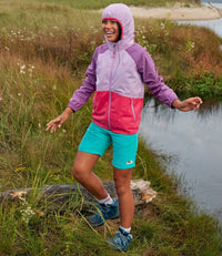 Colorblock windbreaker jacket with hood in purple, pink, and coral worn outdoors