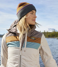 Color block hooded puffer jacket with horizontal stripes in neutral tones, worn outdoors by lake