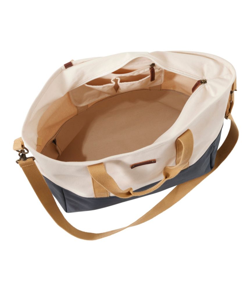 Large canvas tote bag with navy blue bottom and cream top, shown open with interior pockets visible