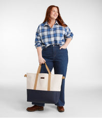 Large tote bag with cream upper section, navy bottom panel, and tan handles held by woman
