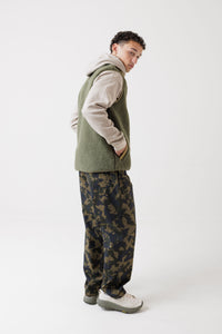Men's sherpa fleece vest in olive green, side view, layered over beige hoodie