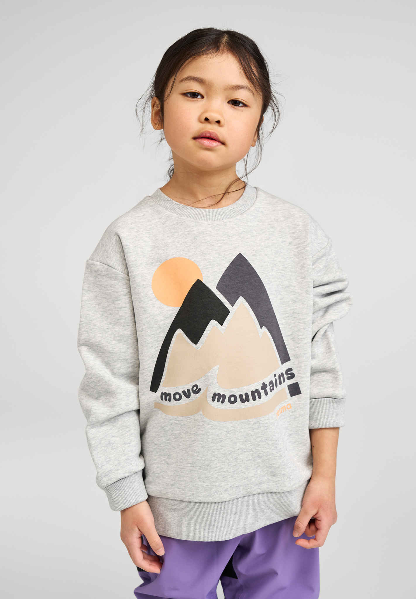 Child wearing grey sweatshirt with colorful mountain design and sun graphic on front