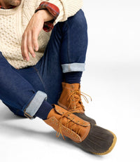Men's lace-up duck boots with tan leather upper and dark brown rubber lower, worn with cuffed jeans