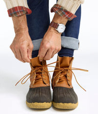 Person lacing up tall duck boots with tan leather upper and dark rubber lower