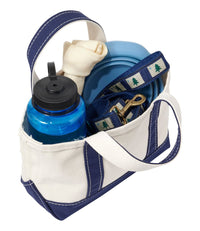Small canvas tote bag with navy trim filled with dog accessories including leash, bowl, bone, and water bottle