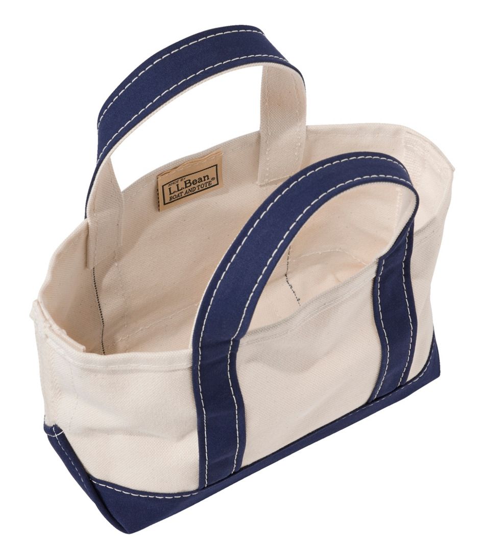 Small canvas tote bag with navy blue handles and trim, open top view showing interior label