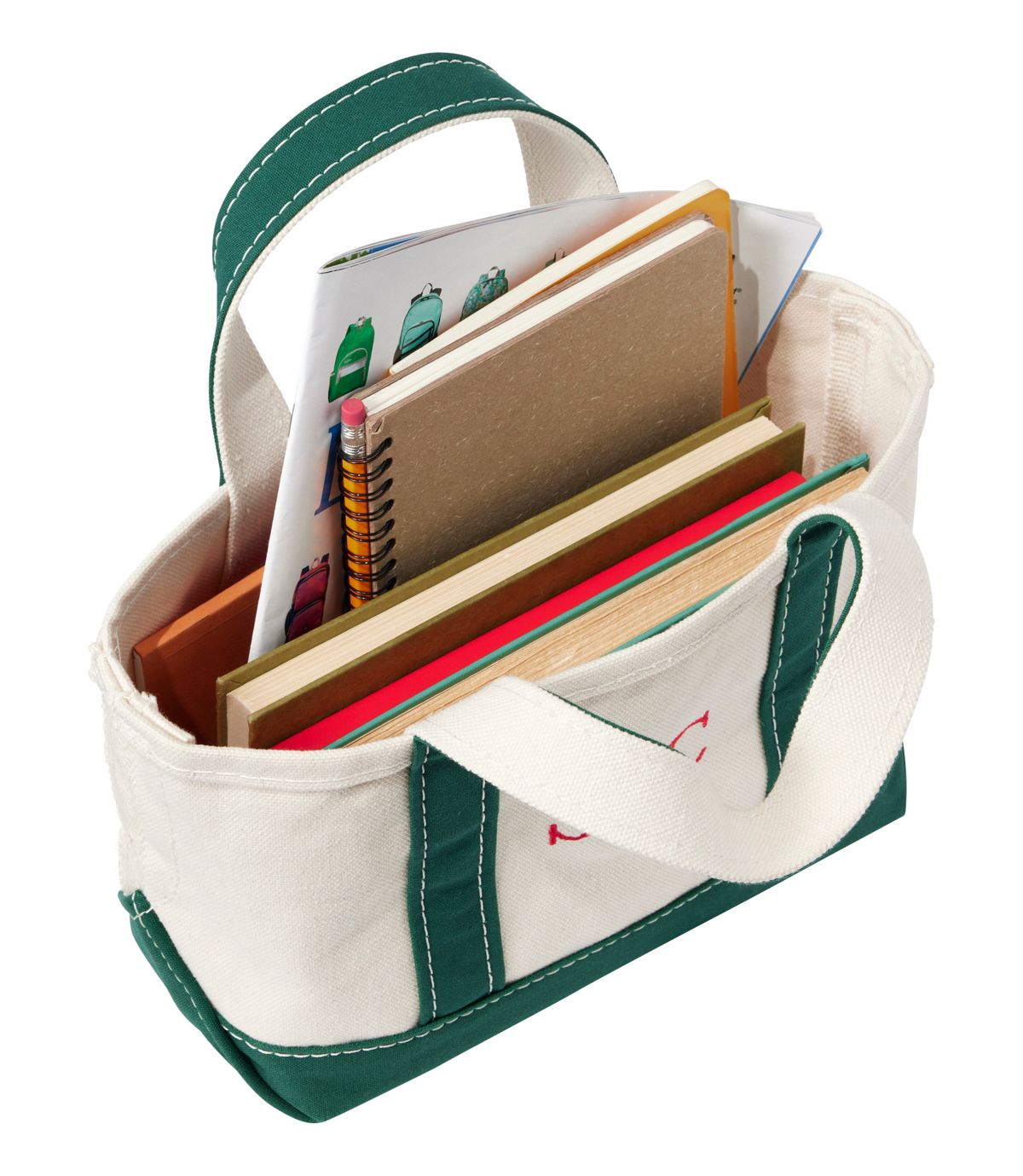 Small canvas tote bag with green handles and trim, filled with books and school supplies