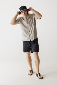 Light tan button-up shirt with collar and chest pocket, worn with navy shorts
