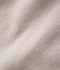 Close-up detail of knit sweater fabric in off-white, showing fine stitch texture and drape