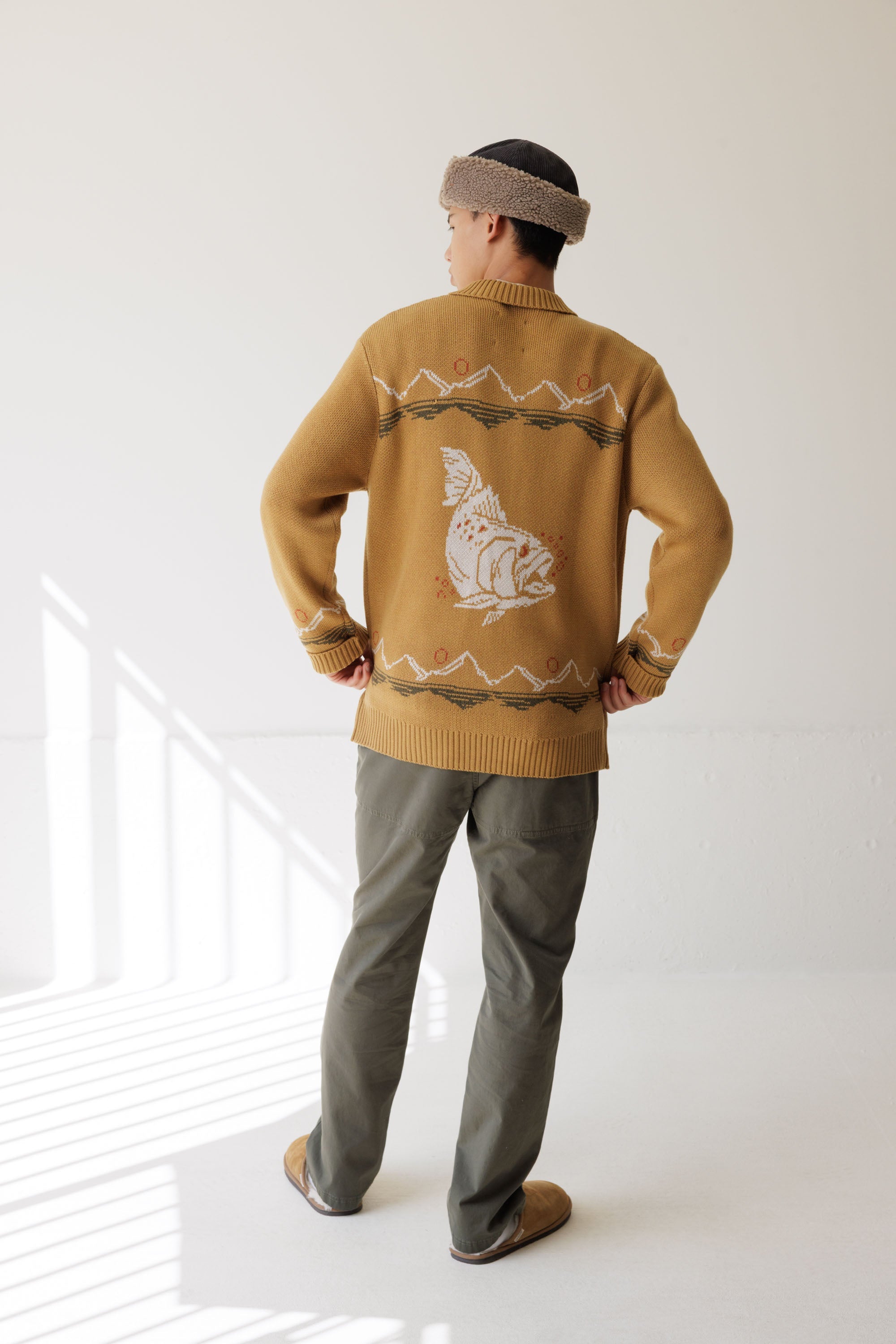 Men's knit sweater with fish graphic on back, worn with olive trousers, back view