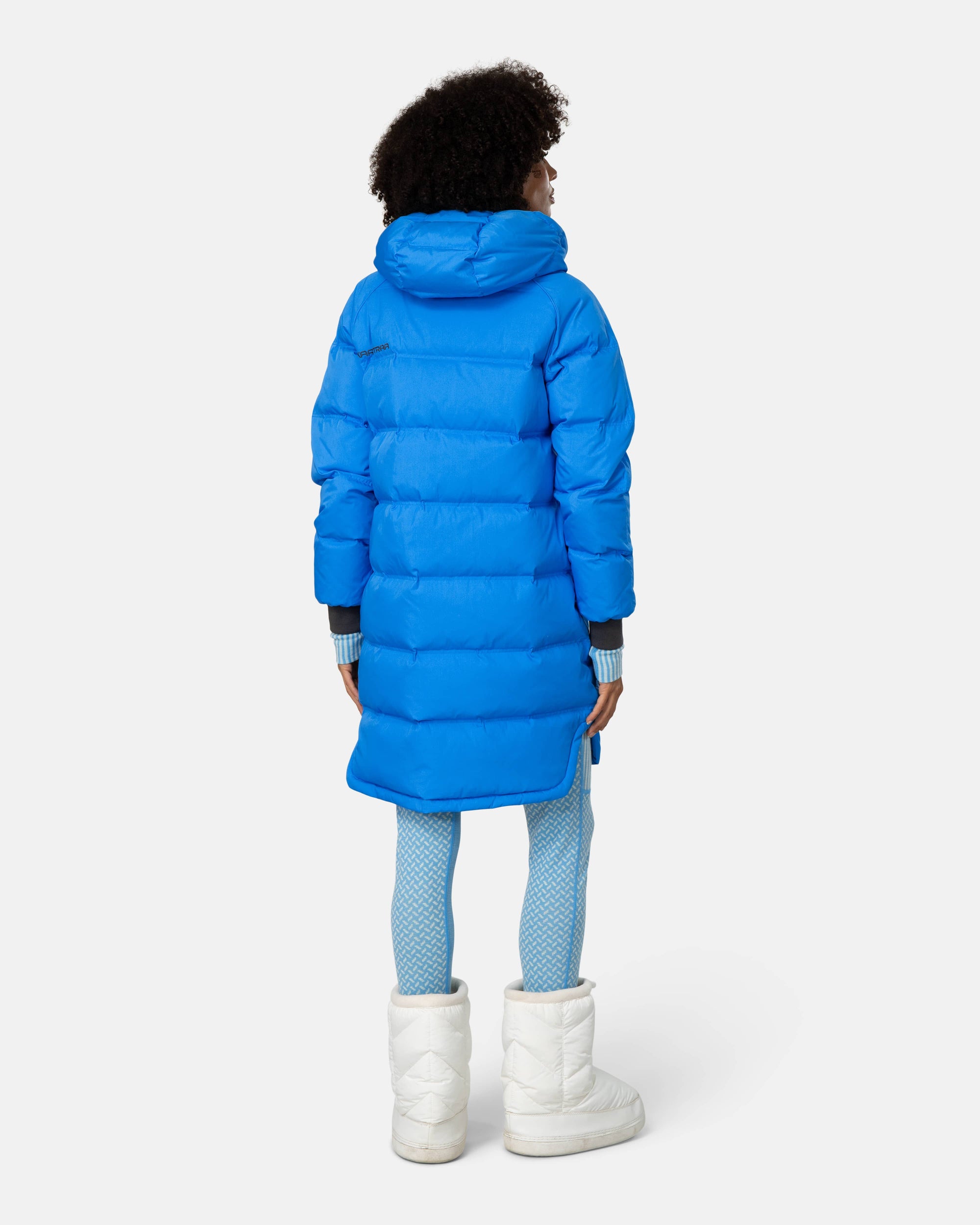 Women's long puffer parka in bright blue, back view, with hood and white snow boots