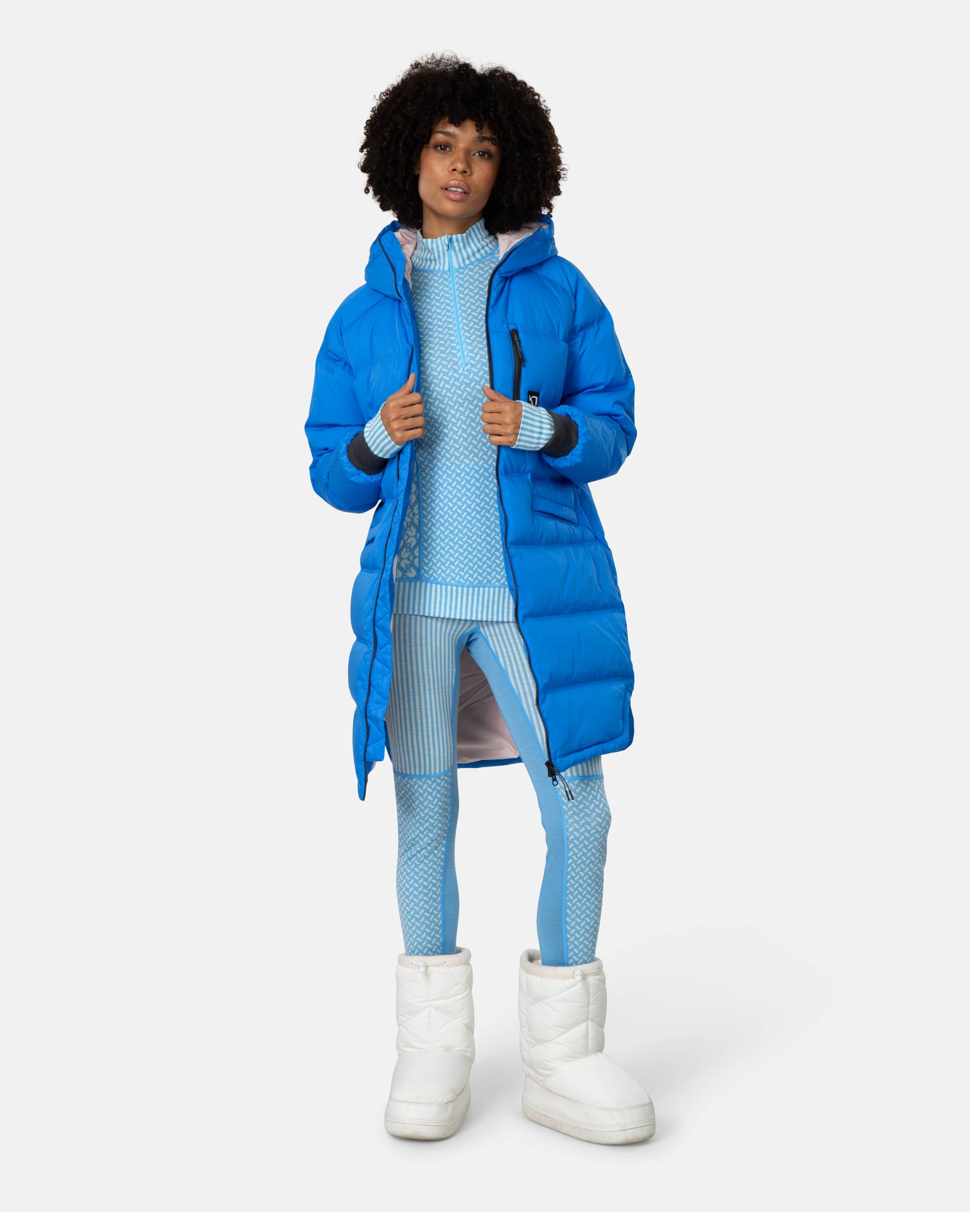 Bright blue long puffer parka with hood, worn open over matching blue knit set, front view