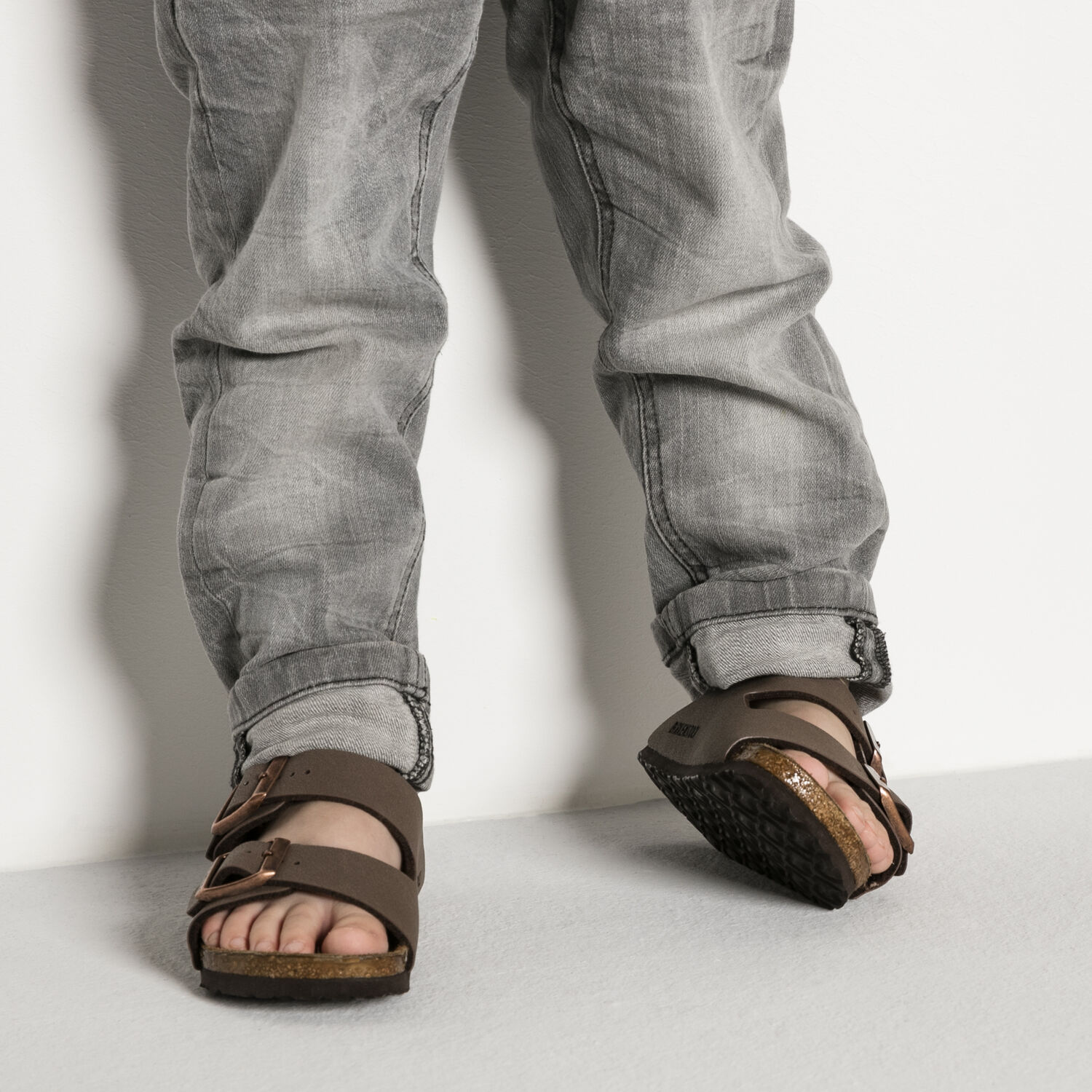 Brown leather sandals with adjustable buckle straps and cork footbed, worn with jeans