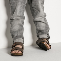 Brown leather sandals with adjustable buckle straps and cork footbed, worn with jeans