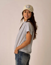 Woman wearing gray pinstriped short-sleeve blouse with jeans and baseball cap
