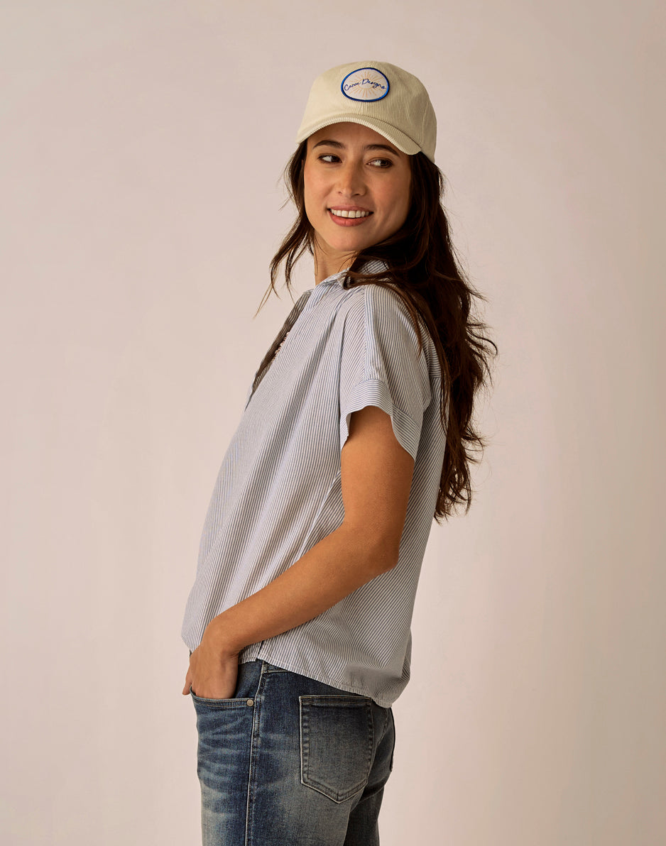 Woman wearing gray pinstriped short-sleeve blouse with jeans and baseball cap
