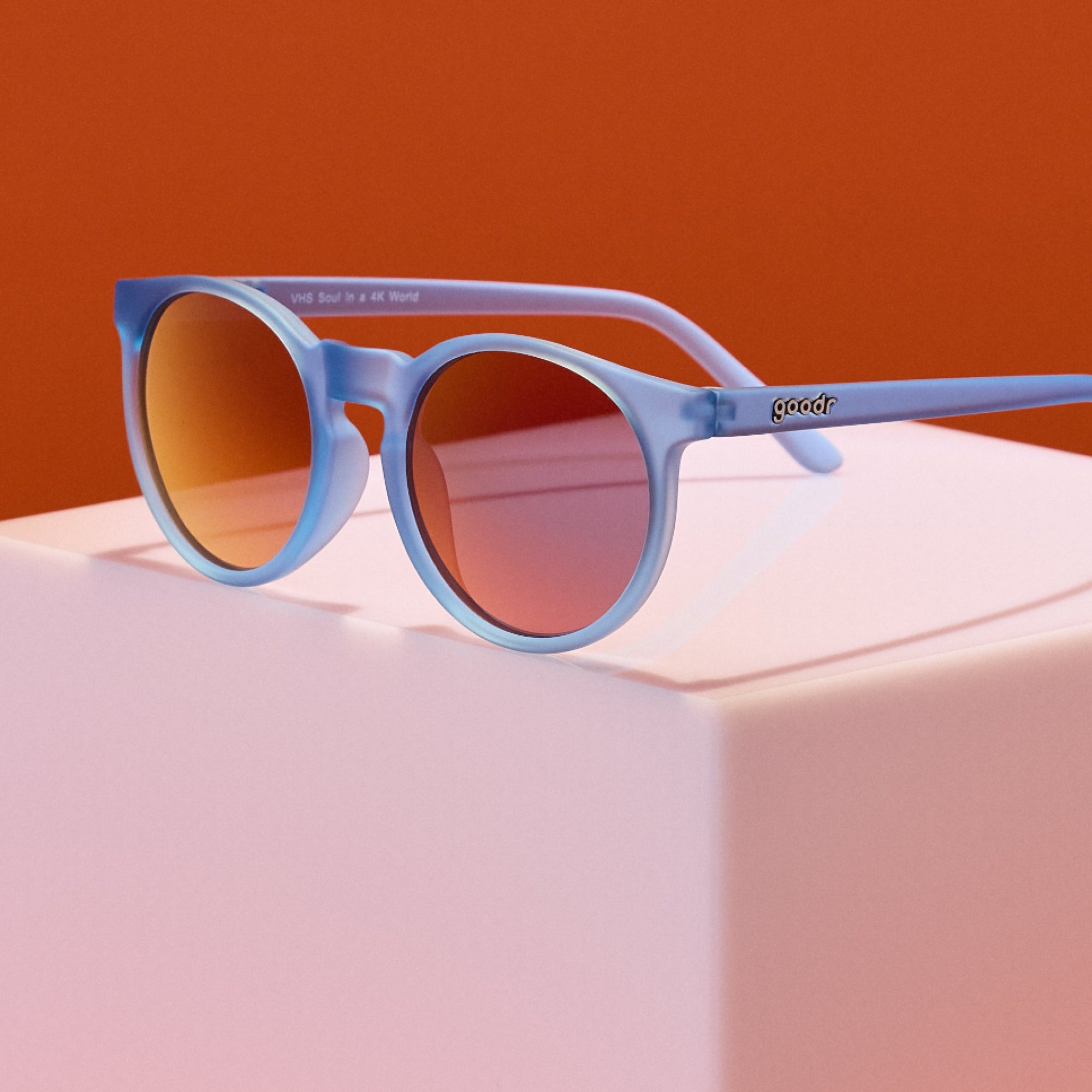 Round frame sunglasses with translucent blue frames and gradient lenses on pink surface