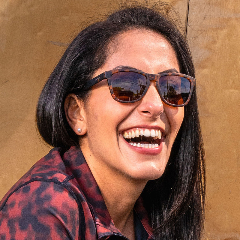 Tortoiseshell sunglasses with dark lenses worn by smiling woman outdoors