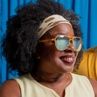 Orange aviator sunglasses worn by person with curly hair and headband, lifestyle photo