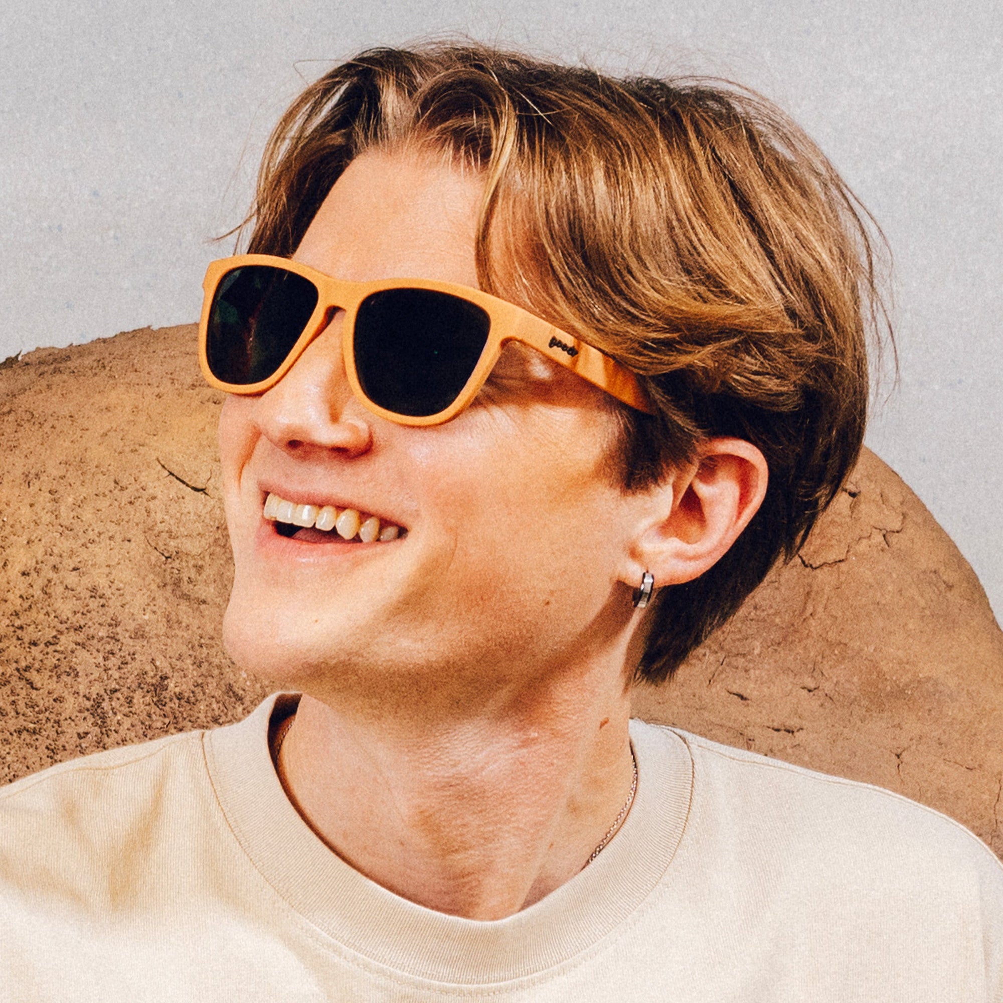 Orange sunglasses with dark lenses worn by person smiling outdoors