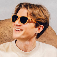 Orange sunglasses with dark lenses worn by person smiling outdoors