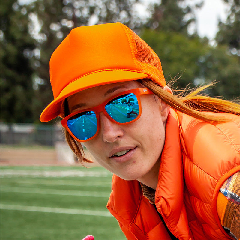 Blue mirrored sunglasses worn by person in orange outfit outdoors