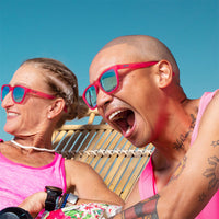 Pink sunglasses with blue lenses worn by laughing couple in beach lifestyle photo