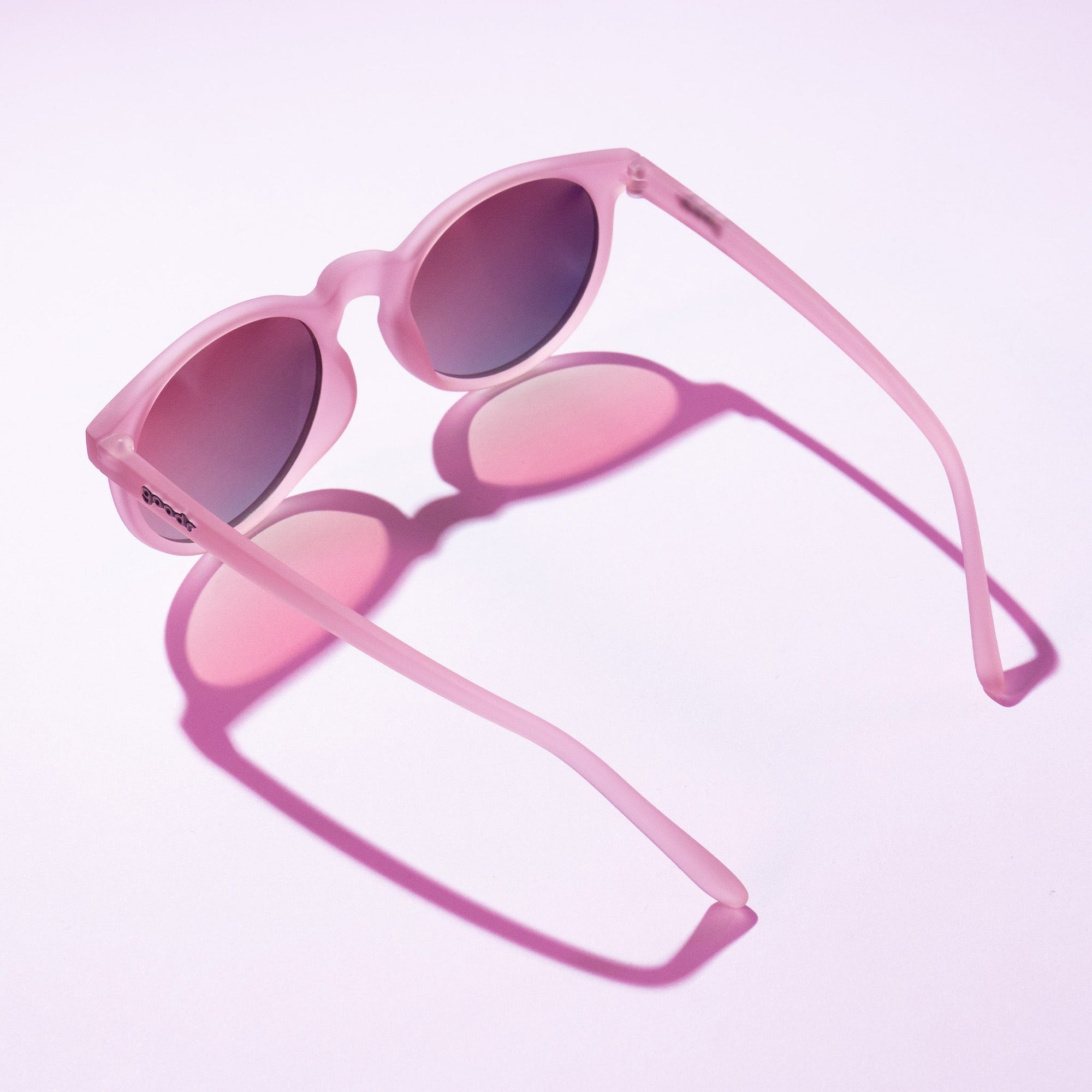 Pink translucent sunglasses with oval lenses shown at an angle against gradient background