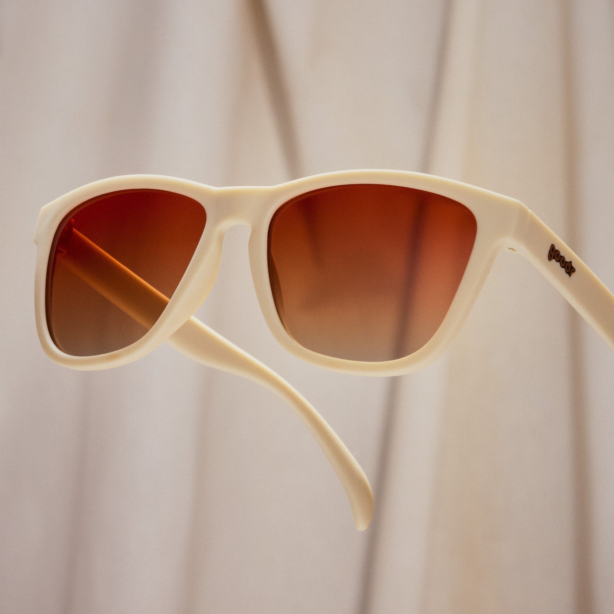 Cream colored sunglasses with brown gradient lenses against soft neutral background