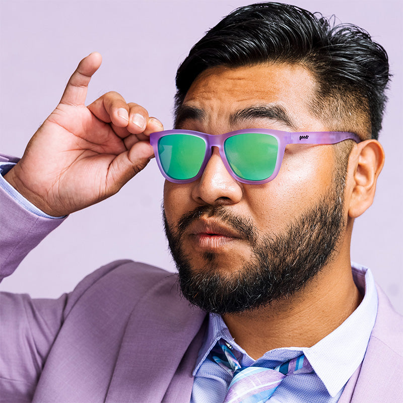 Purple framed sunglasses with green mirrored lenses worn by bearded man in suit