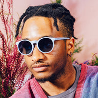 Round sunglasses with white frames and dark lenses worn by person outdoors