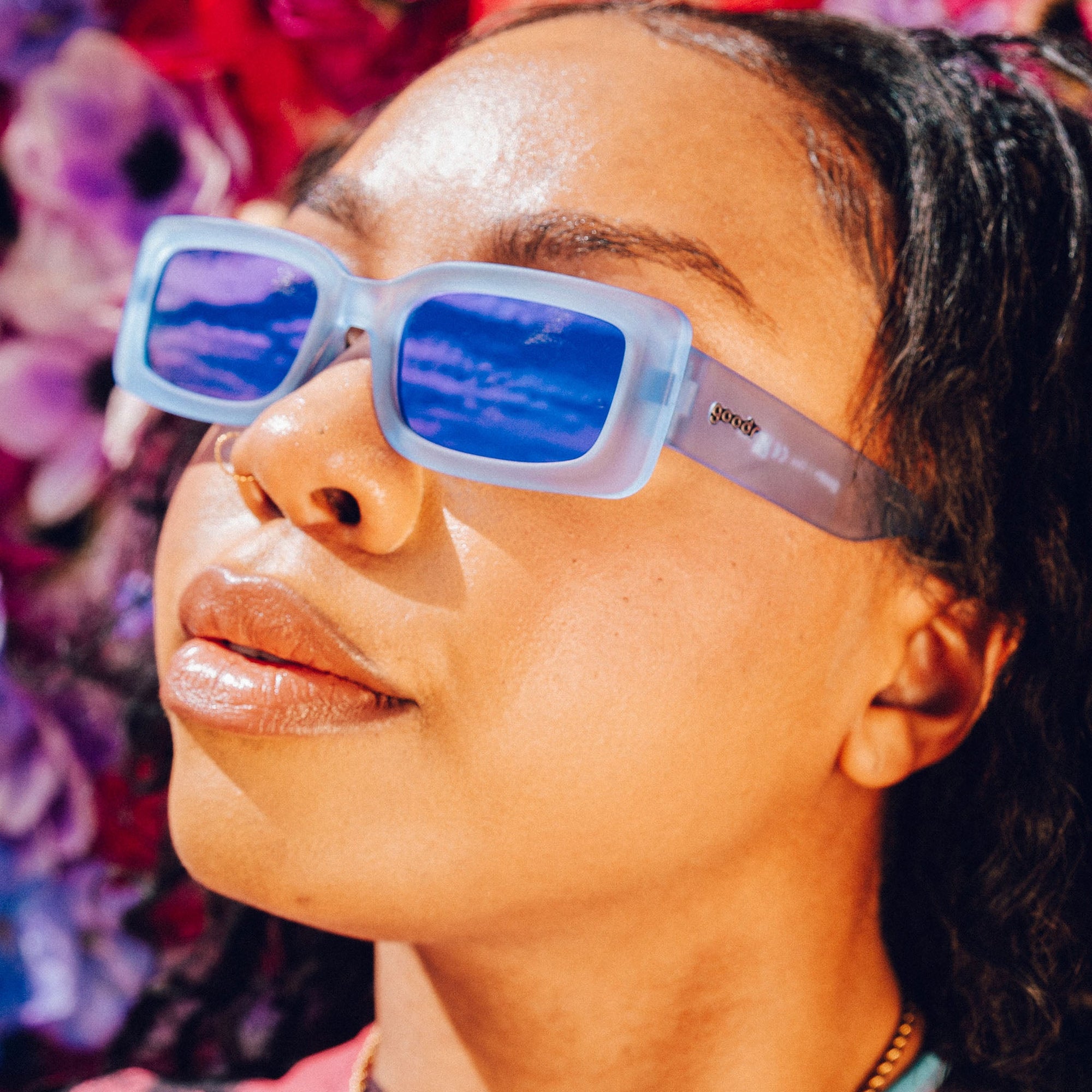 Woman wearing translucent sunglasses with blue lenses, profile view against floral background