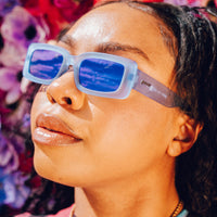 Woman wearing translucent sunglasses with blue lenses, profile view against floral background