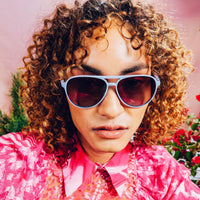 Light blue aviator-style sunglasses with dark gradient lenses worn by person with curly hair