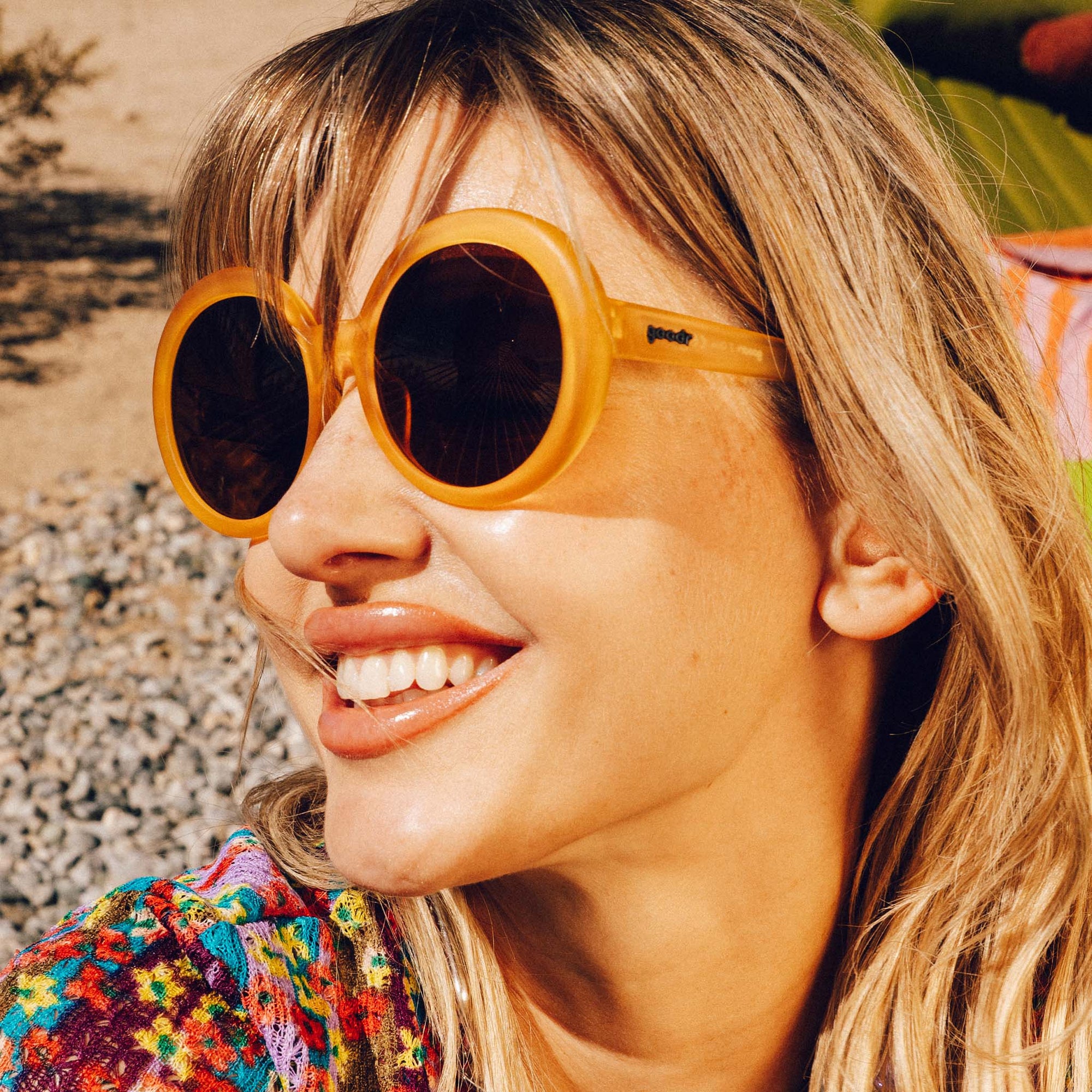 Orange round sunglasses worn by woman with blonde hair smiling outdoors