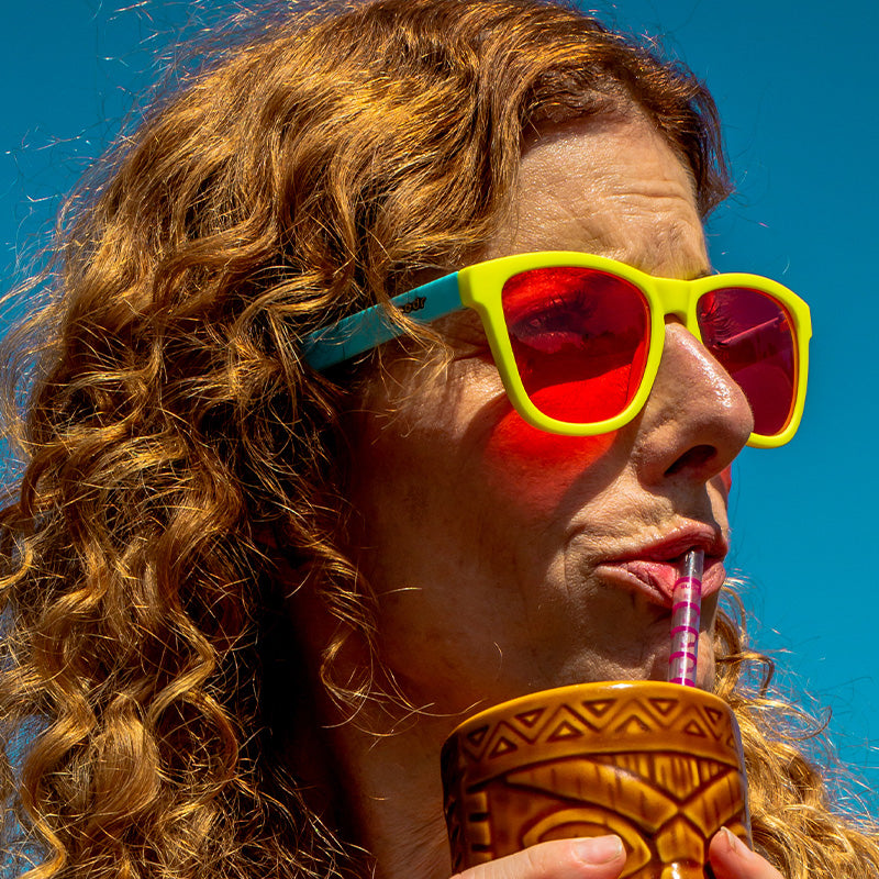 Bright yellow sunglasses with red mirrored lenses worn by person drinking from tiki mug