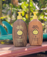 Two pump bottles of sunscreen lotion with wood grain design and yellow dispensers on wooden surface