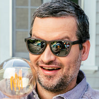 Sunglasses with dark frames and reflective mirrored lenses worn by smiling man