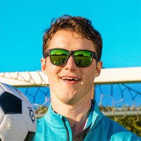 Black sunglasses with green mirrored lenses worn by smiling person outdoors