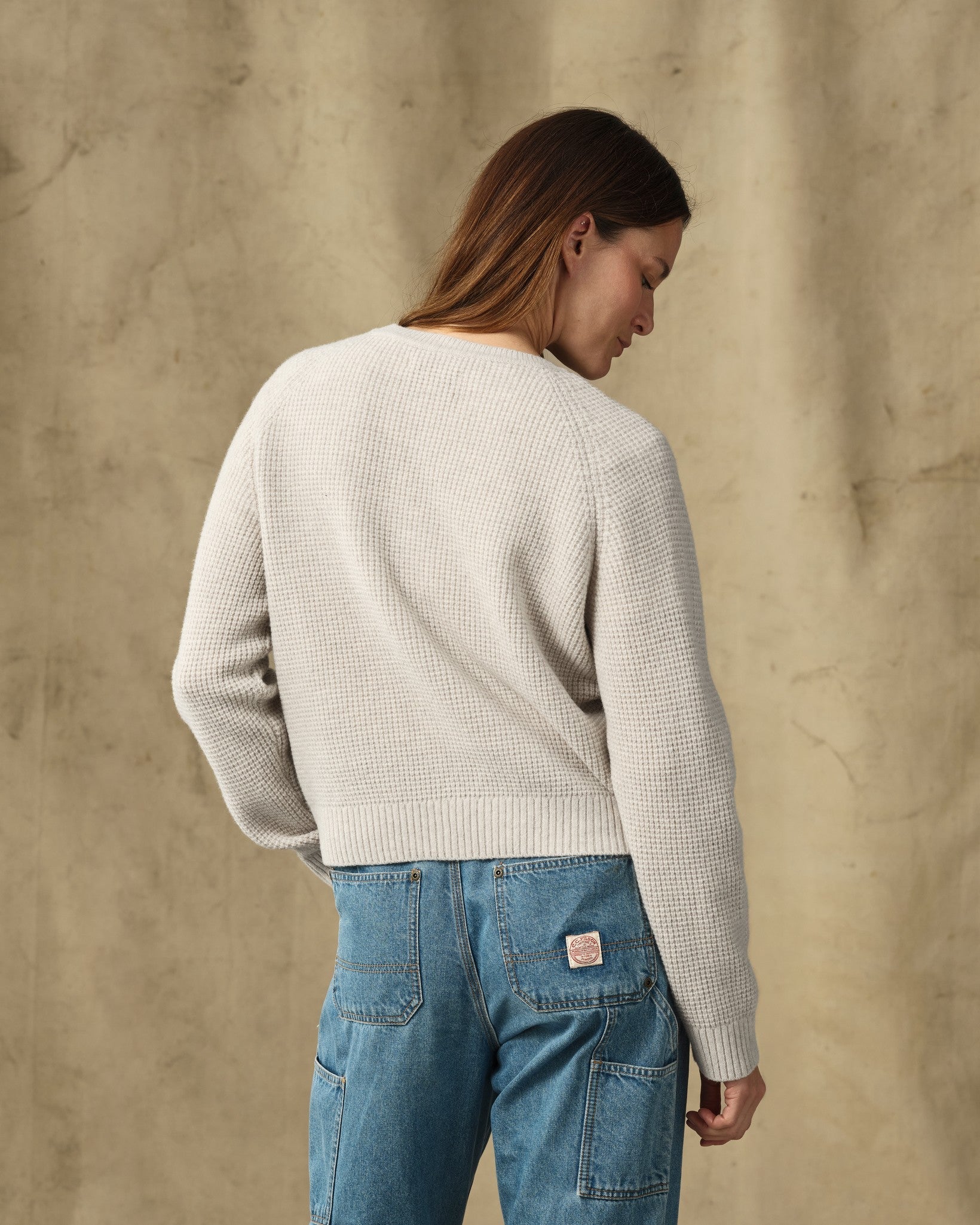 Women's waffle knit crewneck sweater in cream, back view, paired with light wash jeans